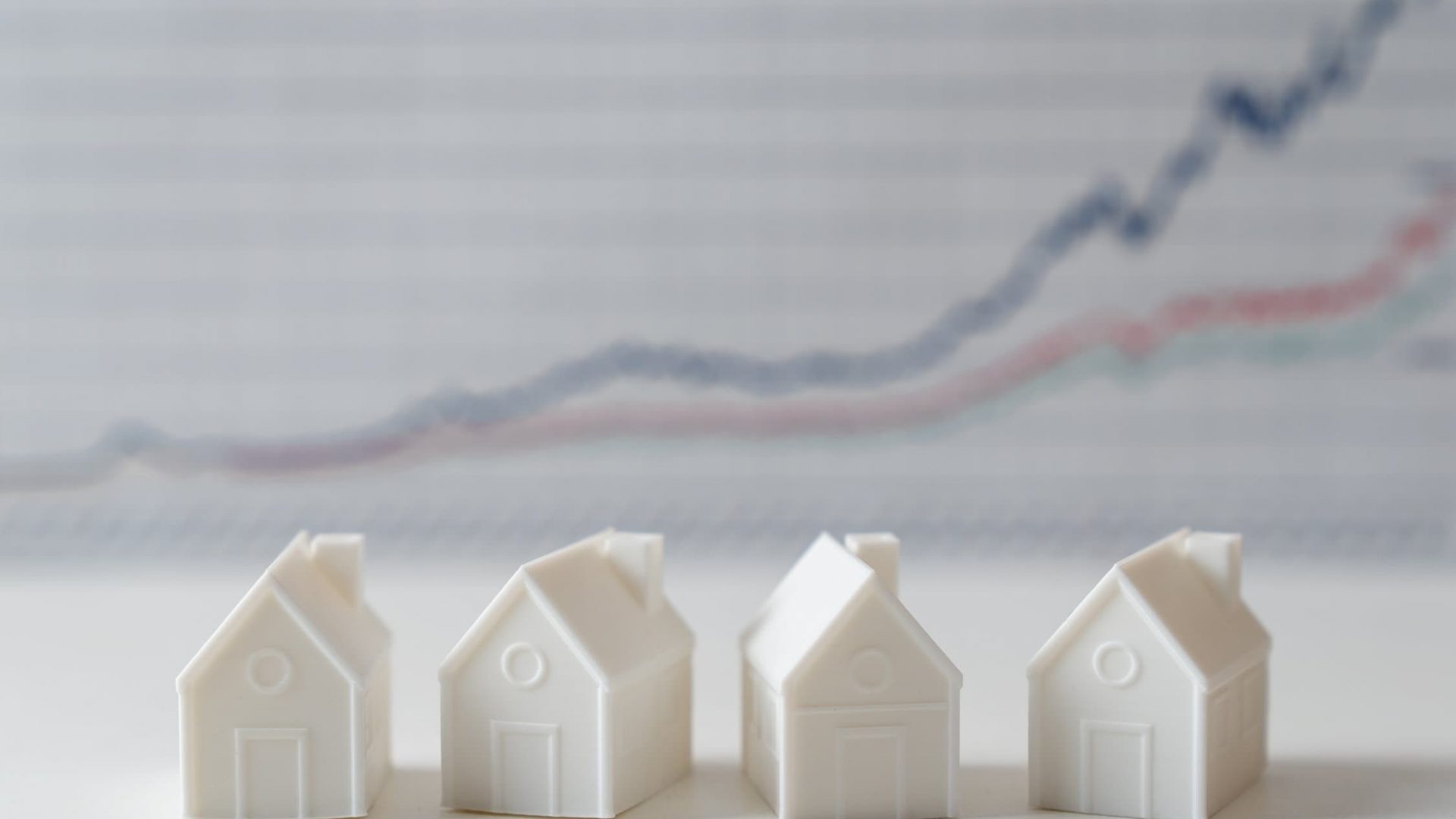 White miniature house models with graph in the background indicating house price is growing or rising high